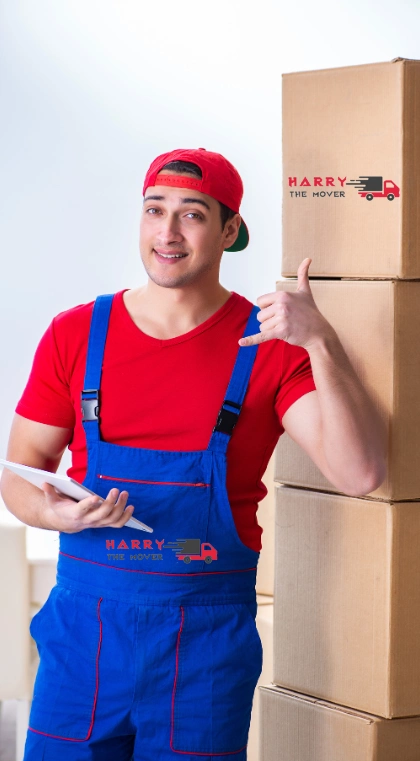 Professional mover from Harry The Mover Melbourne in blue overalls and red uniform giving thumbs up next to a stack of carefully packed moving boxes on a trolley, demonstrating trusted moving services in Melbourne.