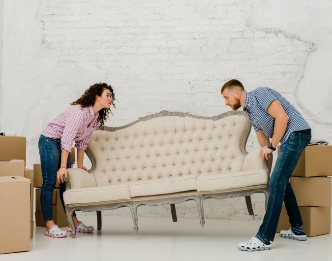 Furniture Removalists Adelaide Couple lifting a sofa during house move with boxes – Furniture Removalists Adelaide.